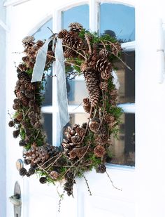 a wreath with pine cones and greenery is hanging on the front door to welcome guests