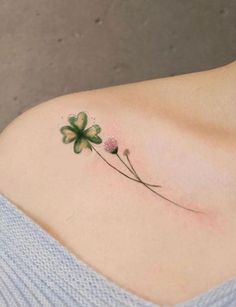 a clover tattoo on the back of a woman's shoulder, with three flowers