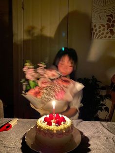 a woman holding a bouquet of flowers in front of a cake with a lit candle on it