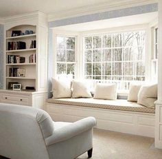 a white chair sitting in front of a window next to a book shelf filled with books