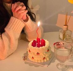 a woman sitting at a table in front of a cake with a lit candle on it