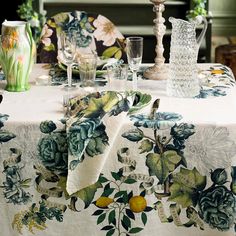 the table cloth is covered with flowers and leaves, along with glass vases on either side