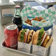 a tray filled with sandwiches and sodas next to two baskets of food on top of a table