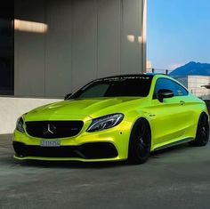 a bright yellow mercedes cla parked in front of a building with mountains in the background