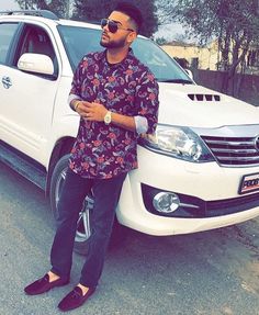 a man standing in front of a white car with sunglasses on it's head