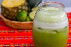 a glass jar filled with green liquid next to a basket of fruit