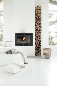 a bedroom with white walls and flooring has a fireplace in the corner next to it