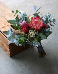 a bouquet of flowers sitting on top of a wooden box filled with leaves and greenery