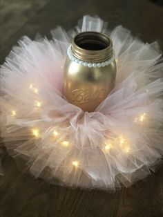 a gold mason jar sitting on top of a white tutule with lights around it