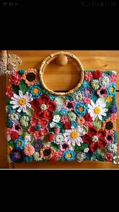 a crocheted bag with flowers on it sitting on a wooden table next to a door