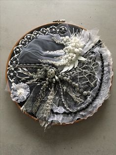 an embroidered piece with lace and flowers on it sitting on top of a wooden plate