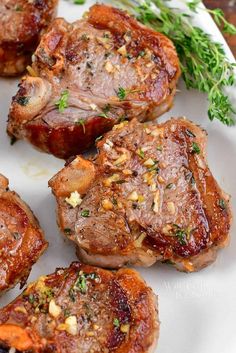 four pieces of meat on a plate with garnishes and seasoning sprigs