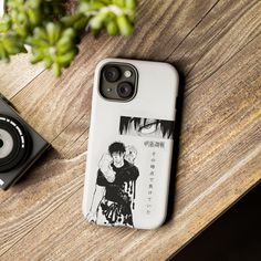 an iphone case sitting on top of a wooden table next to a camera and plant