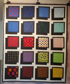 a quilted wall hanging with squares and dots on it