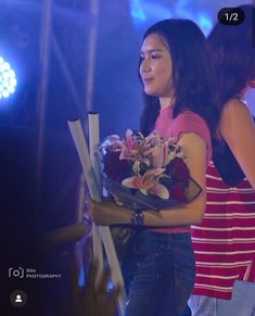 a woman holding flowers in her hand and standing next to other people on the stage