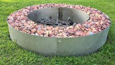 an outdoor fire pit made out of concrete and rocks in the middle of some grass