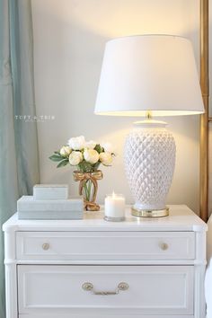 a white lamp sitting on top of a dresser next to a vase filled with flowers