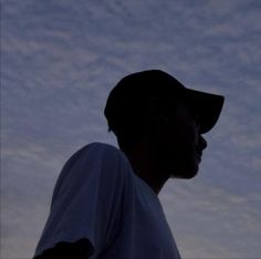 a man wearing a baseball uniform standing in front of a cloudy sky at dusk with his head turned to the side