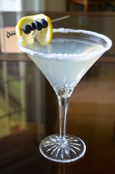 a martini with lemon and black olives on the rim