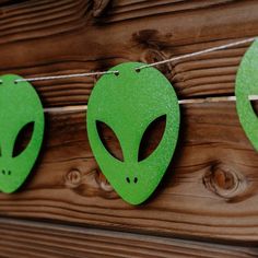 three green alien masks hanging from string on wooden planked wall next to wood fence