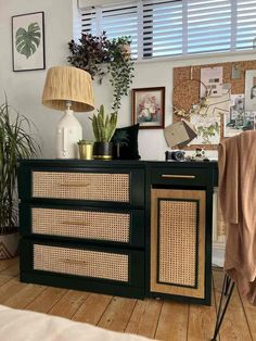 a green cabinet with wicker doors and drawers in a room filled with plants, pictures, and other things