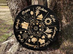 a black and gold colored wheel of the year on a tree in front of some trees