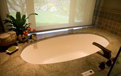 a large bath tub sitting under a window next to a plant and soap dispenser