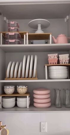 the shelves are filled with dishes and plates in pink, white, and grey colors