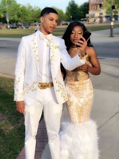 a man in a white suit standing next to a woman wearing a gold and white dress