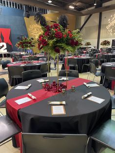 a room filled with tables and chairs covered in black cloths, red tablecloths and centerpieces