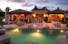 an outdoor pool with patio furniture and umbrellas at dusk, surrounded by palm trees