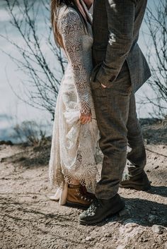 a man and woman standing next to each other on a dirt ground near the water