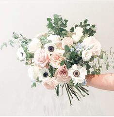 a person holding a bouquet of white and pink flowers with greenery in their hand