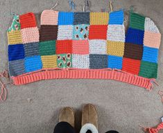 someone's feet are standing in front of a colorful crocheted blanket on the floor