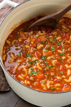 a large pot filled with pasta and meat soup on top of a wooden spoon in it