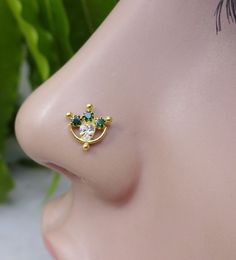 a close up view of a nose piercing with green and white stones on it's side