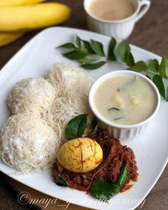 a white plate topped with meat and veggies next to two cups of soup