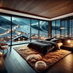 a bedroom with a large window overlooking the snow covered mountains and town lights at night