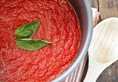 a pot filled with red sauce on top of a wooden table next to a spoon