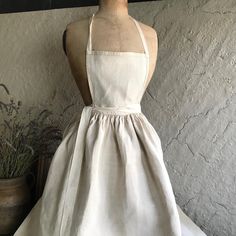 a mannequin wearing a white dress next to a potted plant in front of a wall