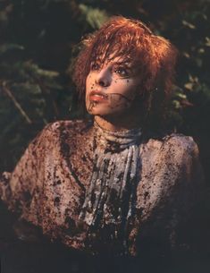 a woman with red hair and makeup is covered in mud