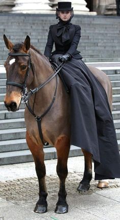 a woman in black riding on the back of a brown and black horse next to some steps