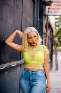 a woman with blonde hair and glasses leaning against a wall on the side of a street