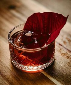 a glass with some liquid and a red flower in it sitting on a wooden table