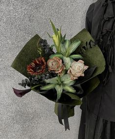 a woman holding a bouquet of flowers in her hand and wearing a black dress with long sleeves