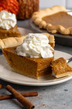 a slice of pumpkin pie on a plate with whipped cream and cinnamon sticks around it