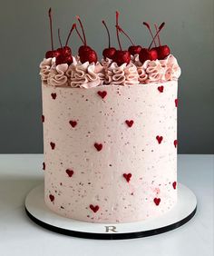 a white cake with pink frosting and hearts on it, topped with cherries