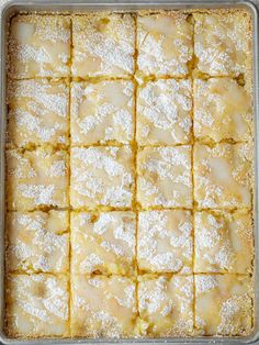 a baking pan filled with dessert squares covered in powdered sugar