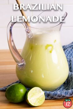 a pitcher filled with lemonade sitting on top of a table next to limes