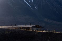 a large building sitting on top of a lush green hillside next to snow covered mountains